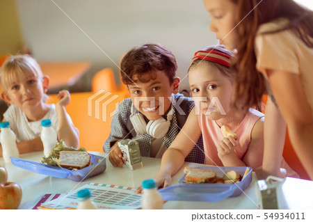 Boy smiling while sitting near girls having lunch together 54934011