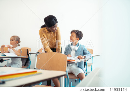 Dark-haired boy smiling while talking to his teacher 54935154