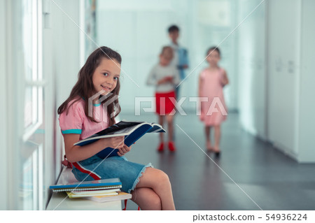 Girl smiling while sitting near window and reading book 54936224
