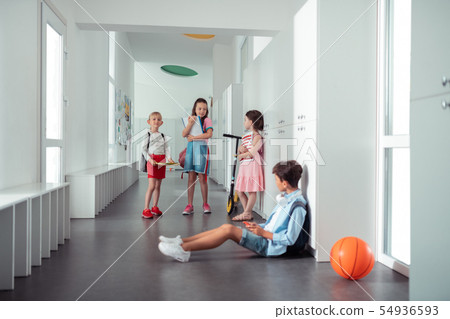 Boy sitting on floor while girls speaking near lockers Boy sitting on floor while girls speaking near lockers 54936593