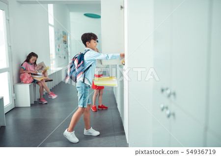 Schoolboy wearing white sneakers opening school locker 54936719