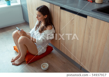 Long-haired woman sitting on the floor and using social media Long-haired woman sitting on the floor and using social media 54937917