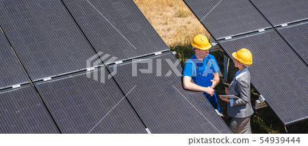 Two people standing amid solar cells in a power plant Two people standing amid solar cells in a power plant 54939444