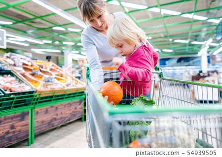 Mother having her toddler riding in shopping cart of supermarket Mother having her toddler riding in shopping cart of supermarket 54939505