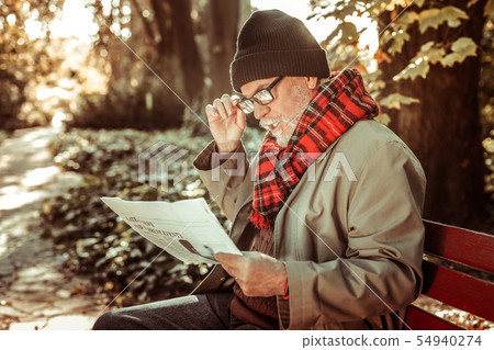 Concentrated aged man attentively reading a newspaper. Concentrated aged man attentively reading a newspaper. 54940274