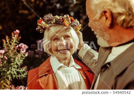 Elderly woman wearing floral wreath and smiling to her husband. Elderly woman wearing floral wreath and smiling to her husband. 54940542