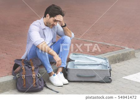 Desperate traveler sitting at international airport with empty suitcase Desperate traveler sitting at international airport with empty suitcase 54941472