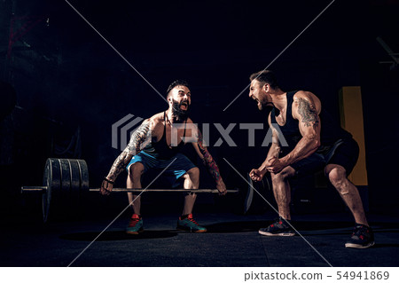 Two muscular bearded tattoed athletes training at gym 54941869