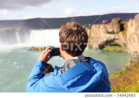 Tourist taking photo of waterfall Godafoss Iceland 54942665
