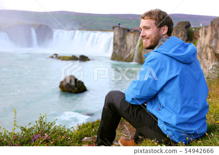 Iceland tourist relaxing by waterfall Godafoss Iceland tourist relaxing by waterfall Godafoss 54942666