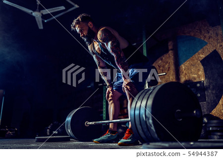 Muscular fitness man preparing to deadlift a barbell over his head in modern fitness center 54944387