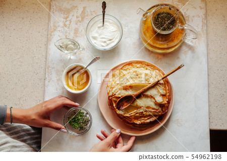 Stack of hot classic Russian thin pancakes. Rustic style. Sour cream, butter, greenery, honey, eggs Stack of hot classic Russian thin pancakes. Rustic style. Sour cream, butter, greenery, honey, eggs 54962198
