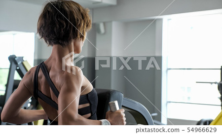 Portrait of woman is making exercises for spine muscles on rowing machine. 54966629