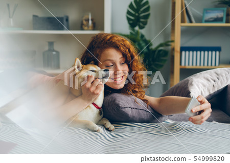 Teenage girl taking selfie with cute puppy using smartphone at home Teenage girl taking selfie with cute puppy using smartphone at home 54999820