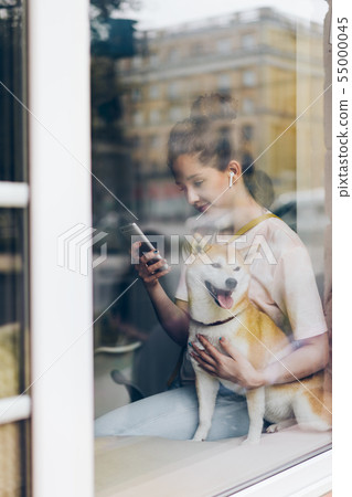 Pretty woman in earphones using smartphone hugging dog in cafe Pretty woman in earphones using smartphone hugging dog in cafe 55000045