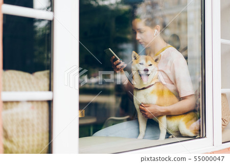 Girl using smartphone listening to music in wireless earphones with dog in cafe Girl using smartphone listening to music in wireless earphones with dog in cafe 55000047