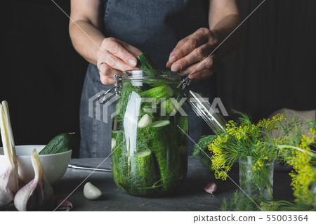 Woman cooking cucumbers with garlic and dill. Woman cooking cucumbers with garlic and dill. 55003364