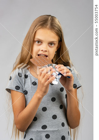 A ten-year-old girl eats a chocolate bar A ten-year-old girl eats a chocolate bar 55003754