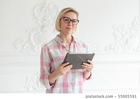 Charming short-haired woman in glasses holds tablet in her hands and smiling Charming short-haired woman in glasses holds tablet in her hands and smiling 55005591