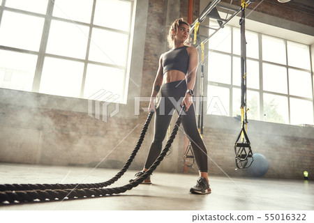 CrossFit training. Young athletic woman with perfect body doing crossfit exercises with a rope in CrossFit training. Young athletic woman with perfect body doing crossfit exercises with a rope in 55016322