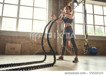 Functional training. Young athletic woman with perfect body doing crossfit exercises with a rope in 55016325