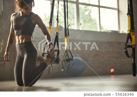 Young athletic woman in sports clothing adjusting trx fitness straps while training in the gym. Young athletic woman in sports clothing adjusting trx fitness straps while training in the gym. 55016340