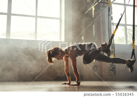 TRX Training. Young athletic woman in sports clothing training legs with trx fitness straps in the 55016345