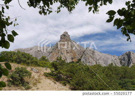 A wide rocky ridge with green trees at its foot ag A wide rocky ridge with green trees at its foot ag 55020177