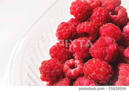 Close-up ripe juicy and delicious raspberry in a plastic transparent dish on a light background Close-up ripe juicy and delicious raspberry in a plastic transparent dish on a light background 55029504