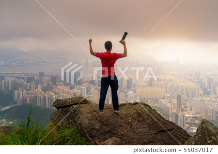 A photographer hiking and looking at city on rock, 55037017