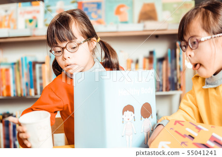 Unusual young girls sitting together and observing informative book Unusual young girls sitting together and observing informative book 55041241