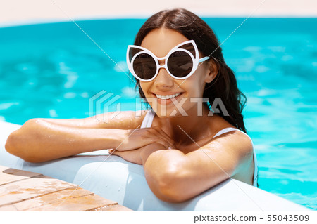 Woman wearing sunglasses smiling in swimming pool Woman wearing sunglasses smiling in swimming pool 55043509