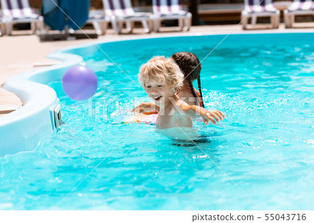 Brother laughing while playing ball with sister in pool 55043716