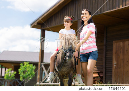 Mother and her daughter sitting on the horse enjoying warm weather Mother and her daughter sitting on the horse enjoying warm weather 55044301