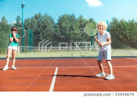 Cheerful brother feeling happy playing tennis with sister Cheerful brother feeling happy playing tennis with sister 55044679