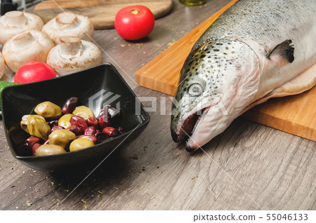 Close-up keta fish, whole on the cutting board of the kitchen table next to olives tomatoes and 55046133