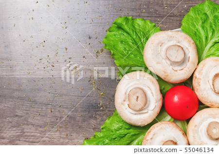 Closeup of white mushrooms with green salad leaves with tomato on a dark wooden table. Vegetarian 55046134