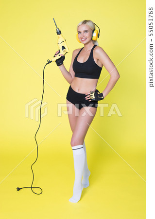 Young sexy woman in headphones holding a drill. Woman builder. Young sexy woman in headphones holding a drill. Woman builder. 55051768