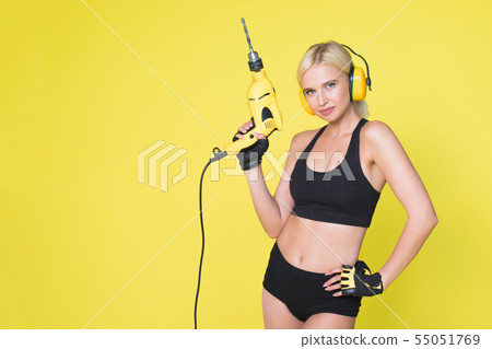Young sexy woman in headphones holding a drill. Woman builder. Young sexy woman in headphones holding a drill. Woman builder. 55051769