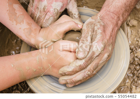 two pairs of hands mold something from clay on a 55054482
