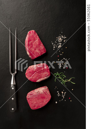 Raw fillet beef steaks with salt, pepper, rosemary, and a carving fork on a black background with 55062081