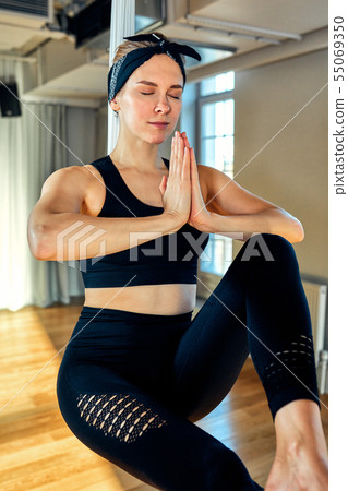 Aerial yoga A beautiful girl aerial yoga trainer shows a variety of exercises on hanging lines in a 55069350