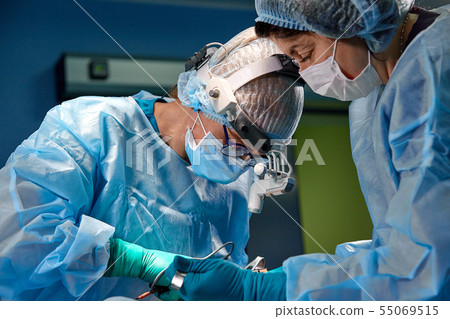 Surgeon performing cosmetic surgery in hospital operating room. Surgeon in mask wearing loupes 55069515