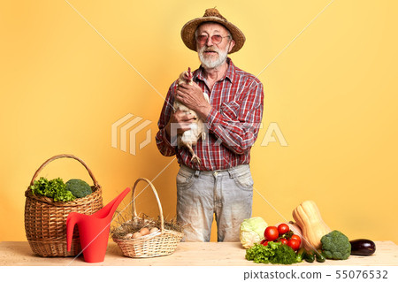 Mature gardener standing with hen behind counter with fresh vegetables 55076532