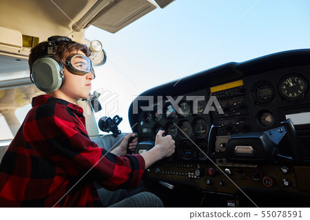 boy sitting in airpalne cabin in headset, pretending he is a pilot 55078591