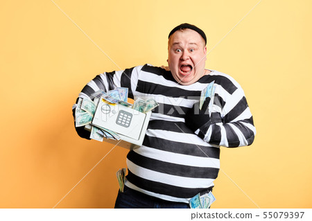 cheerful fat criminal holding a safe full of money. robbery concept. 55079397
