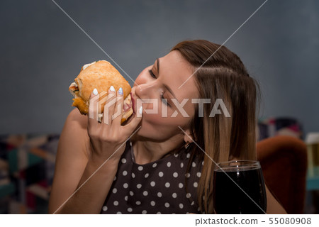 Young woman eating hamburger in restaurant. Close up face with closed eyes Young woman eating hamburger in restaurant. Close up face with closed eyes 55080908