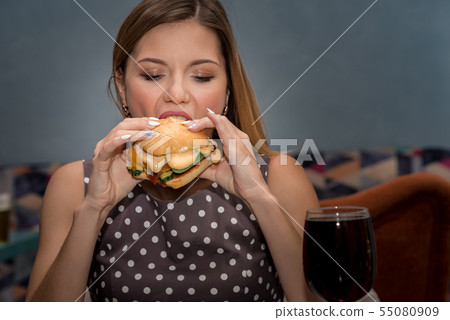 Young woman eating hamburger in restaurant. Close up face with closed eyes 55080909
