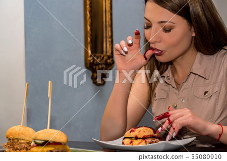 Young woman eating hamburger in restaurant. Licking fingers Young woman eating hamburger in restaurant. Licking fingers 55080910