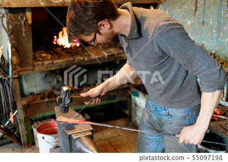 Blacksmith forging red-hot metal with hammer. 55097198